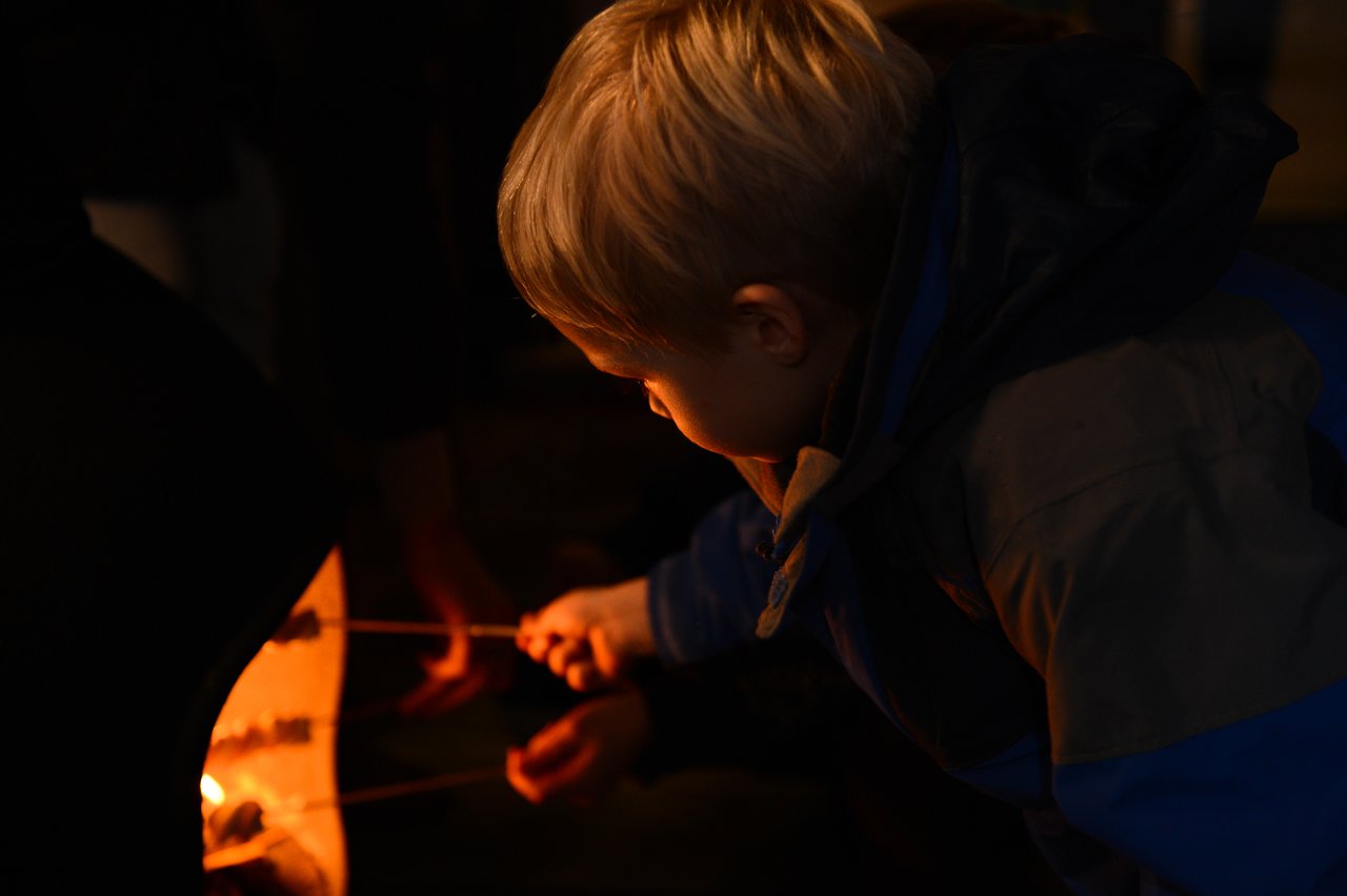 A child in a winter jacket roasts marshmallows over an open fire at a New Year's party.