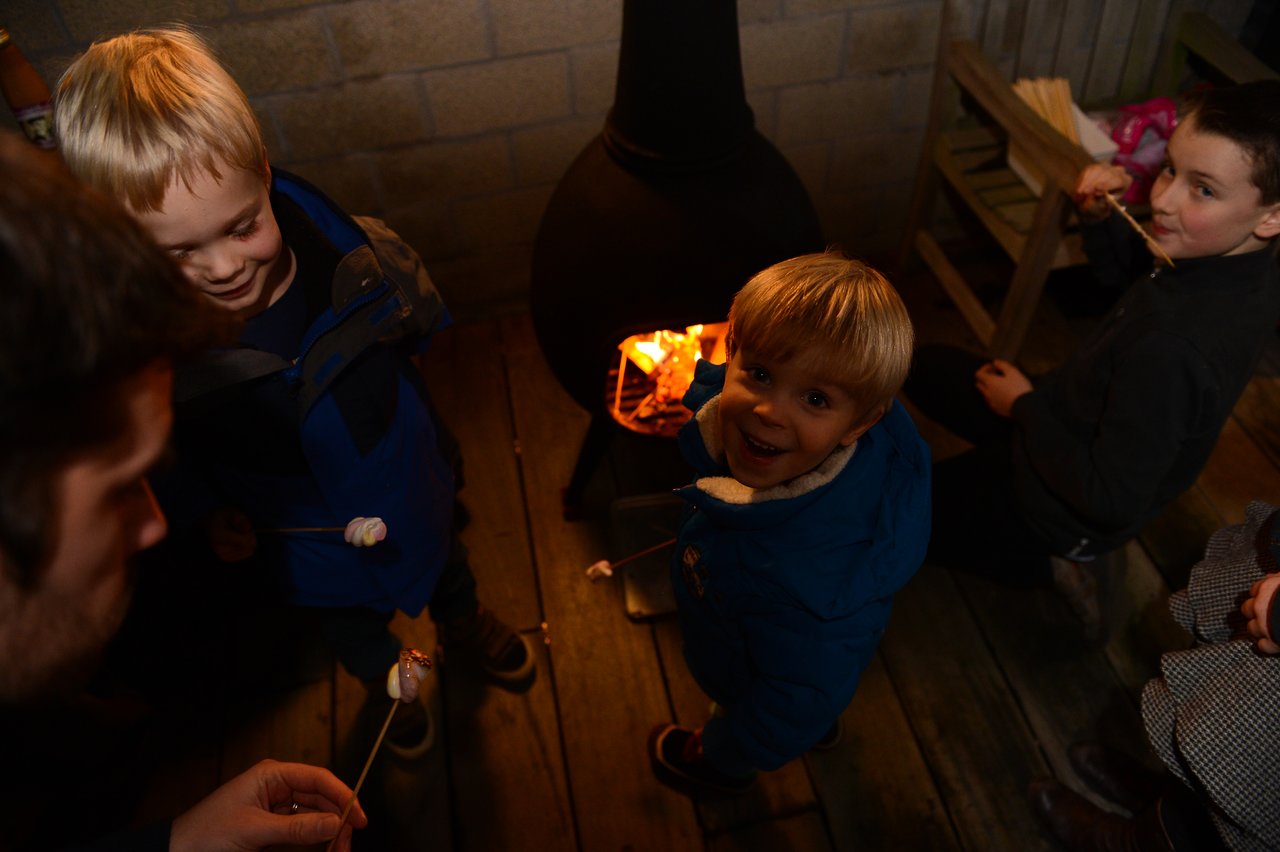 Children roast marshmallows over a small fire, smiling and enjoying the moment at a New Year's party.