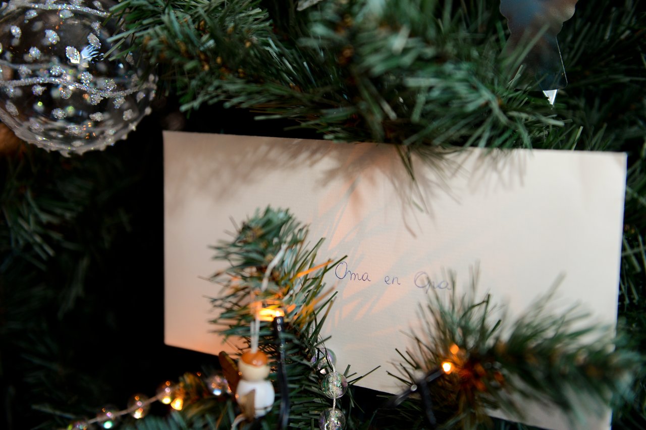 A Christmas tree with a decorated ornament and a letter tucked between the branches, addressed to "Oma en Opa.