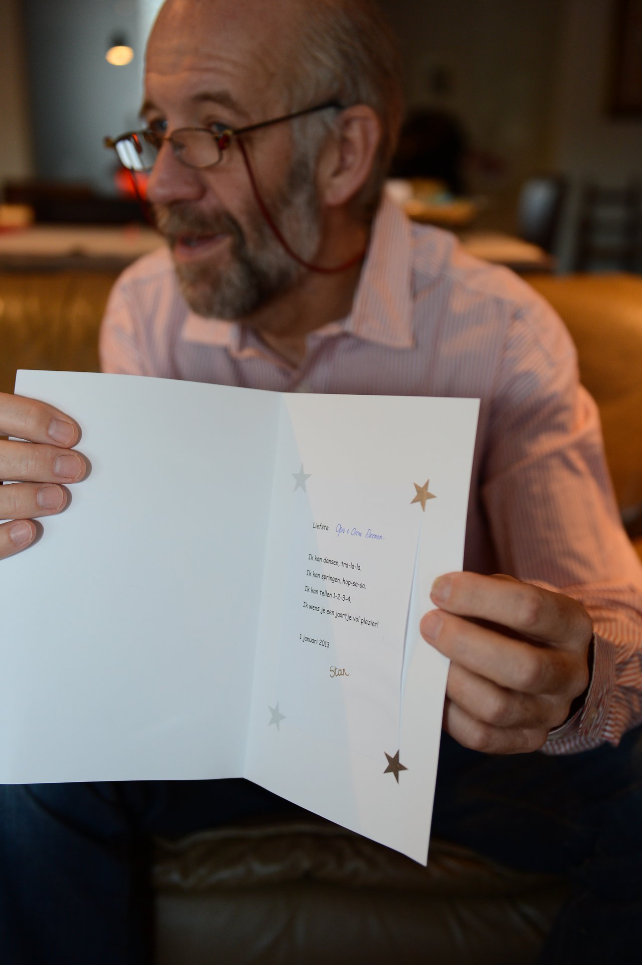 A man in glasses and a striped shirt holds up an open greeting card with a message inside.
