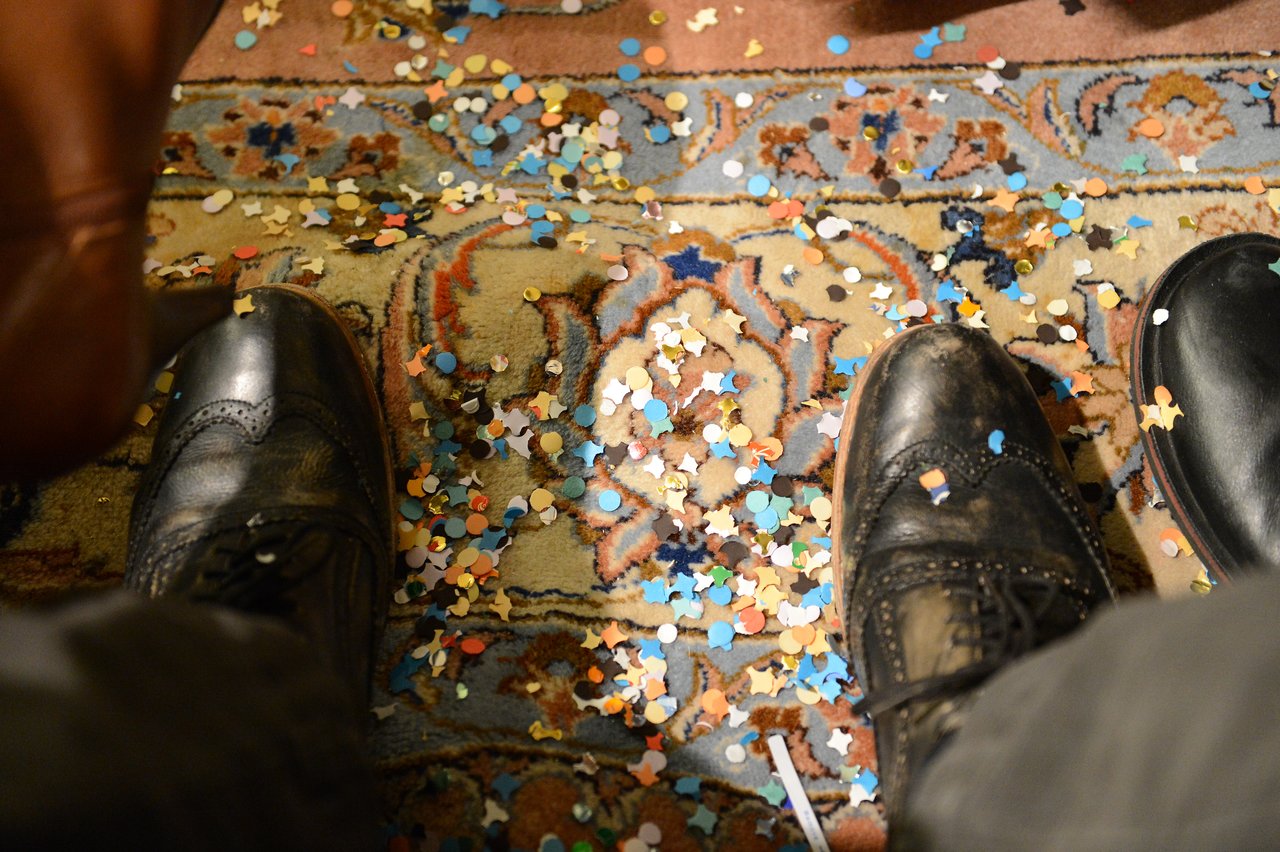 Shoes on a patterned rug covered in colorful confetti, likely after a New Year's celebration.