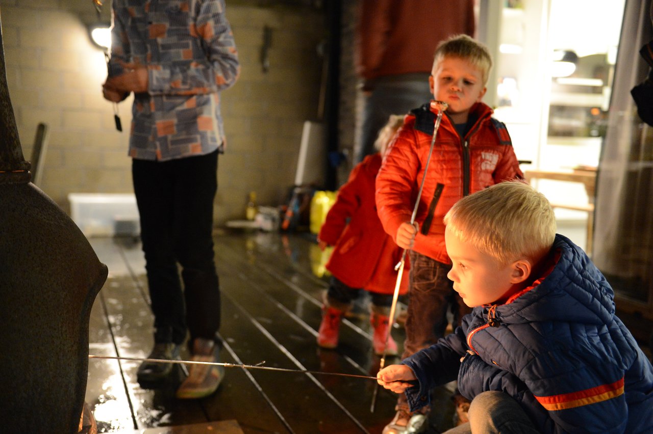Children in warm jackets roast marshmallows over an outdoor fire during a New Year's celebration at night.