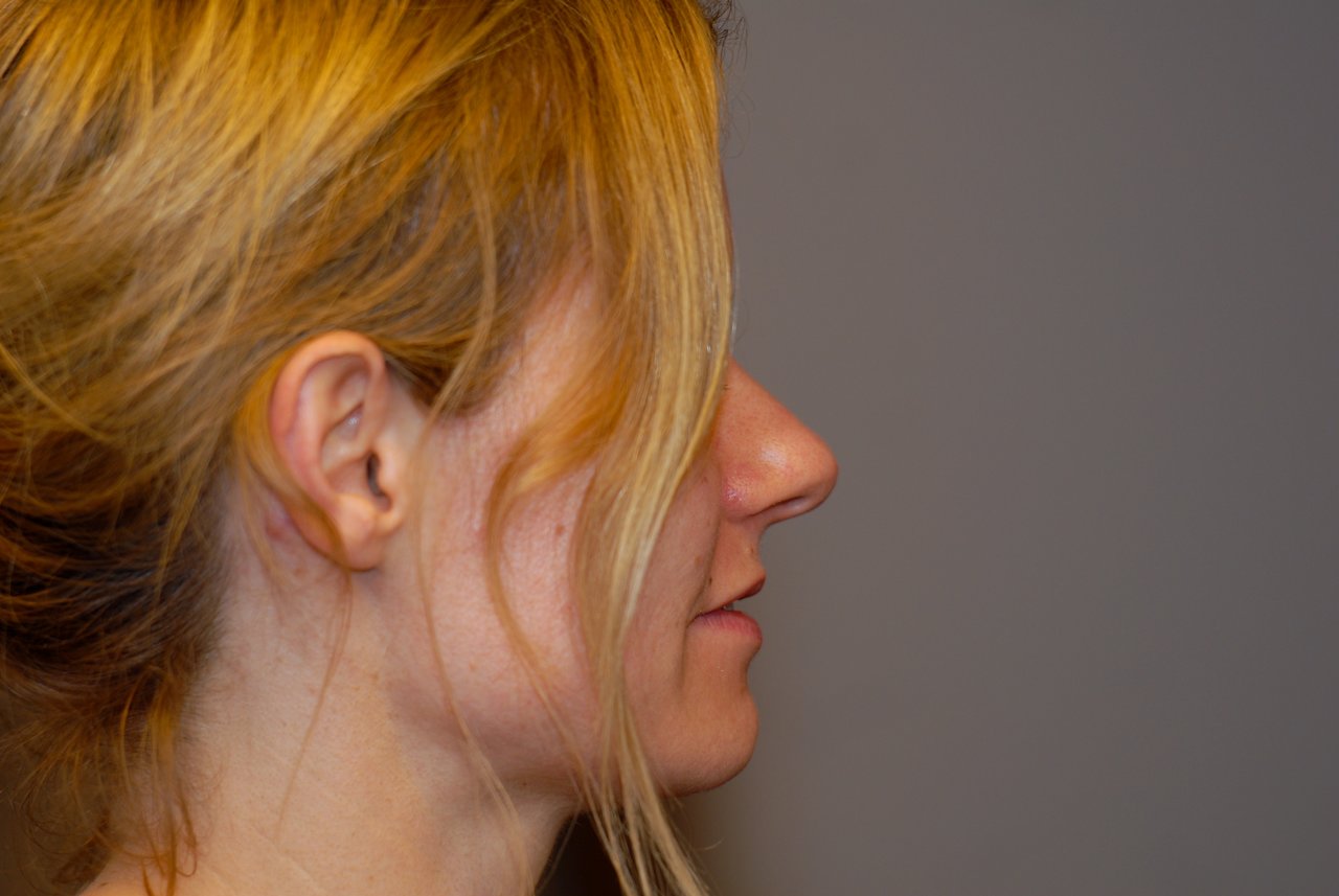 A woman with blonde hair is shown in profile, looking to the right in an indoor setting.