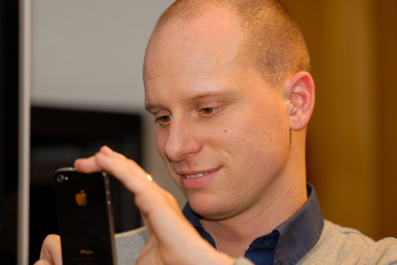 A man smiles while taking a photo with his smartphone at a New Year's Eve party.