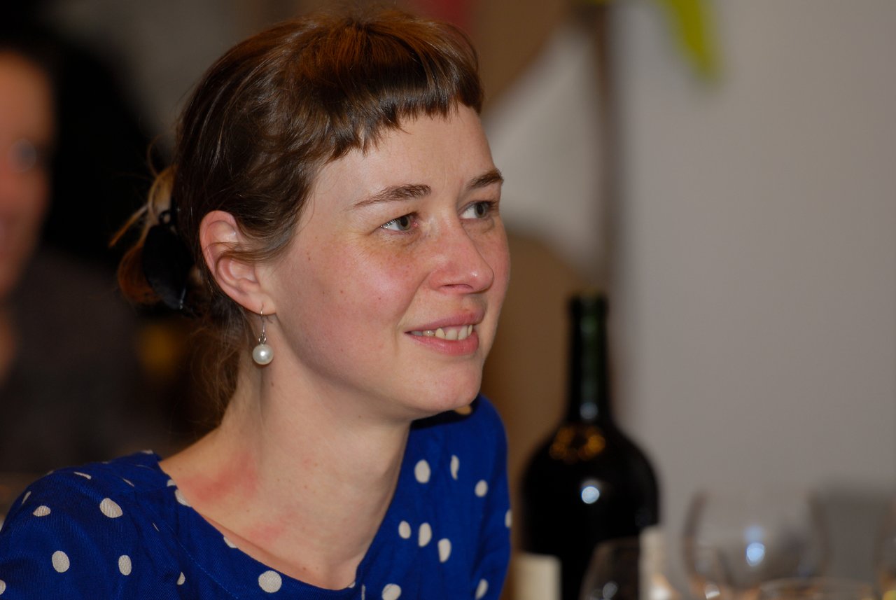 A woman in a blue polka-dot dress smiles while sitting at a table during a New Year's Eve party.