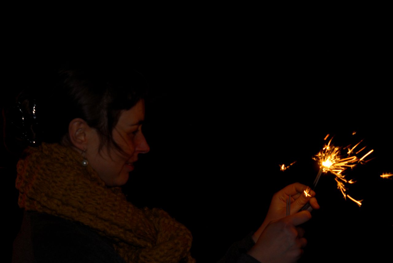 A person holds and lights sparklers in the dark, celebrating during a New Year's Eve party.