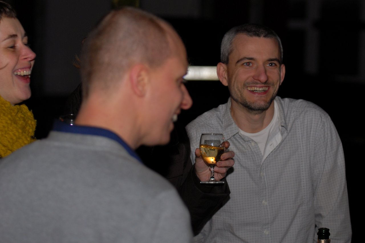A group of people laughing and chatting at a party, with one person holding a glass of wine.