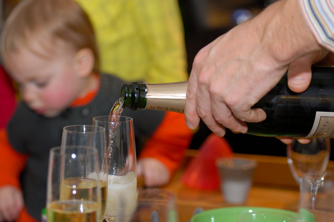 A person pours champagne into glasses at a party, with a child in the background.