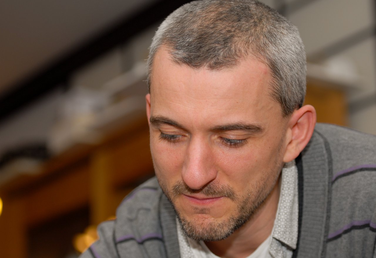 A man in a gray sweater looks down with a focused expression at a New Year's Eve party.