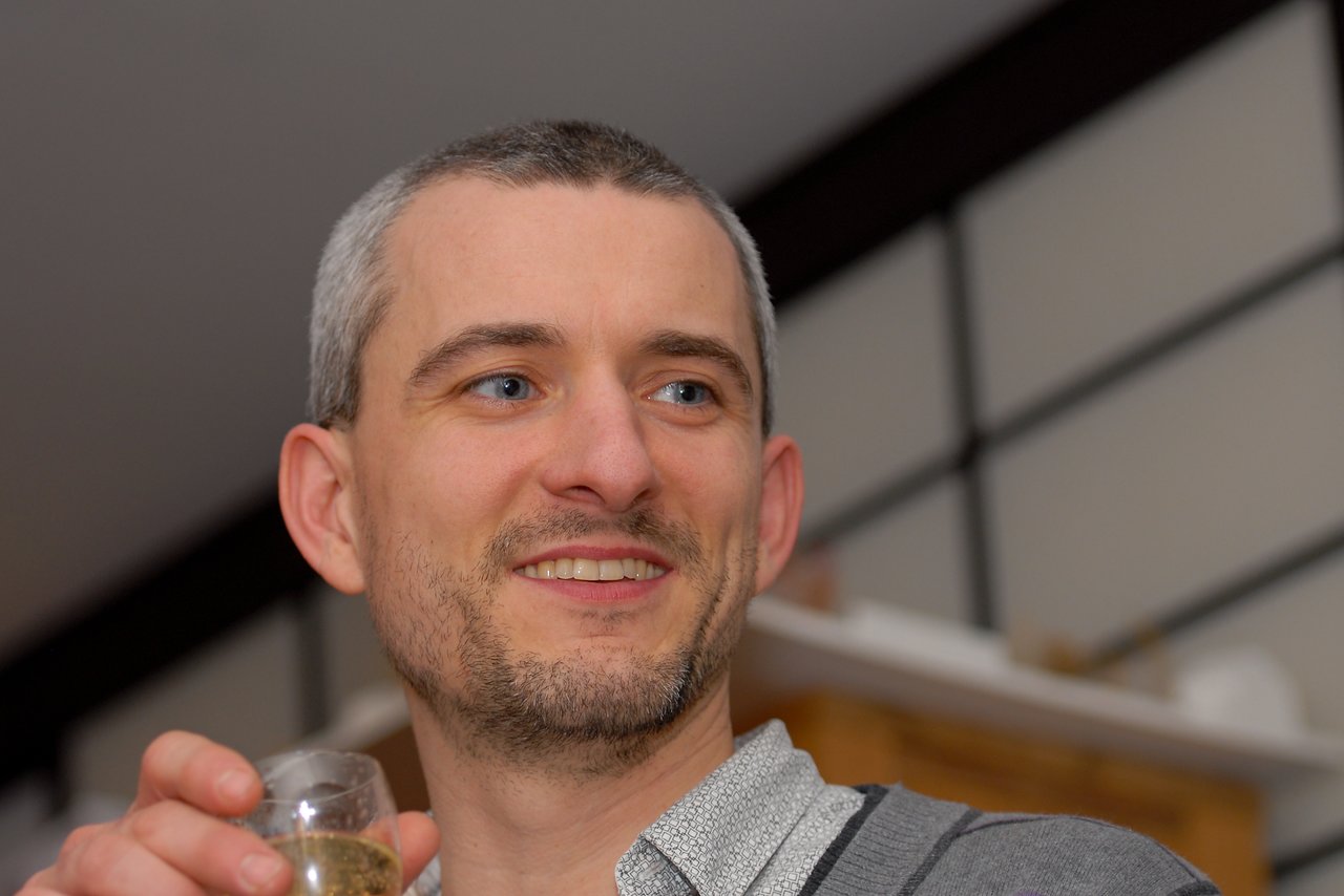 A man smiles while holding a glass of champagne at a New Year's Eve party.
