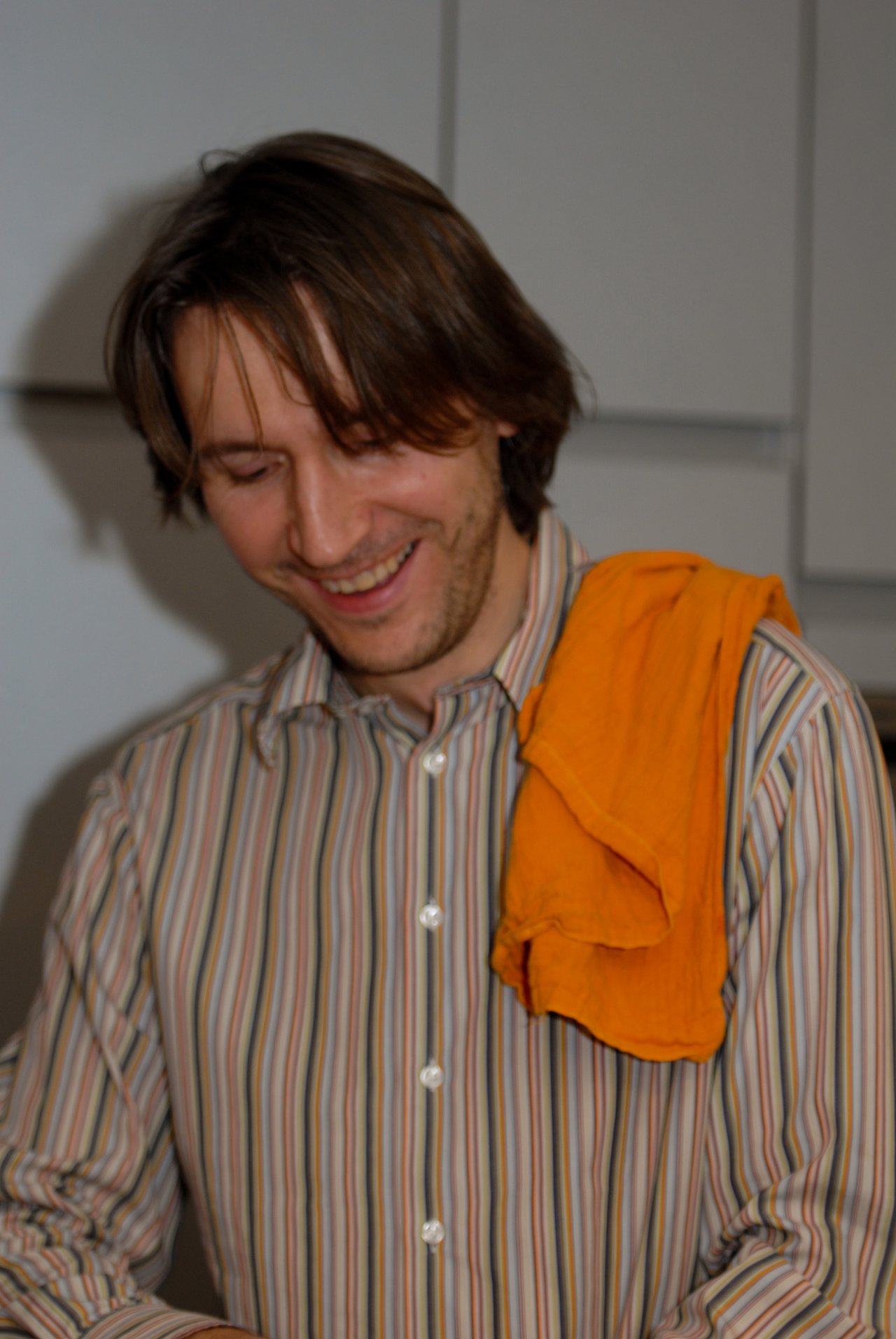 A man in a striped shirt smiles with an orange cloth draped over his shoulder at a party.