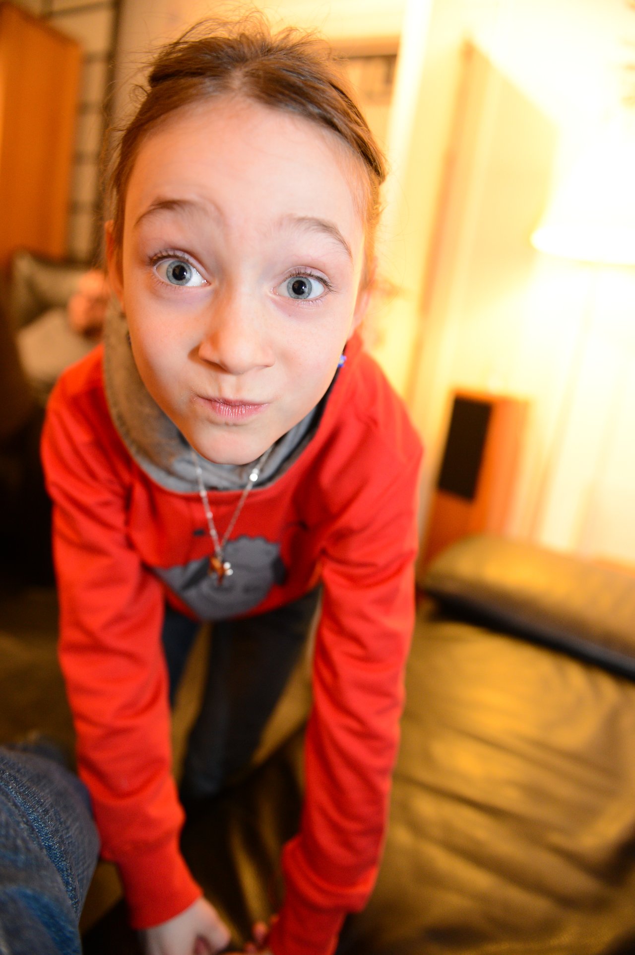 A child in a red hoodie leans forward, making a playful facial expression at the camera during a party.
