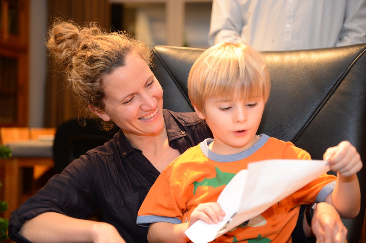 A woman smiles while a young boy in an orange shirt excitedly looks at a piece of paper.