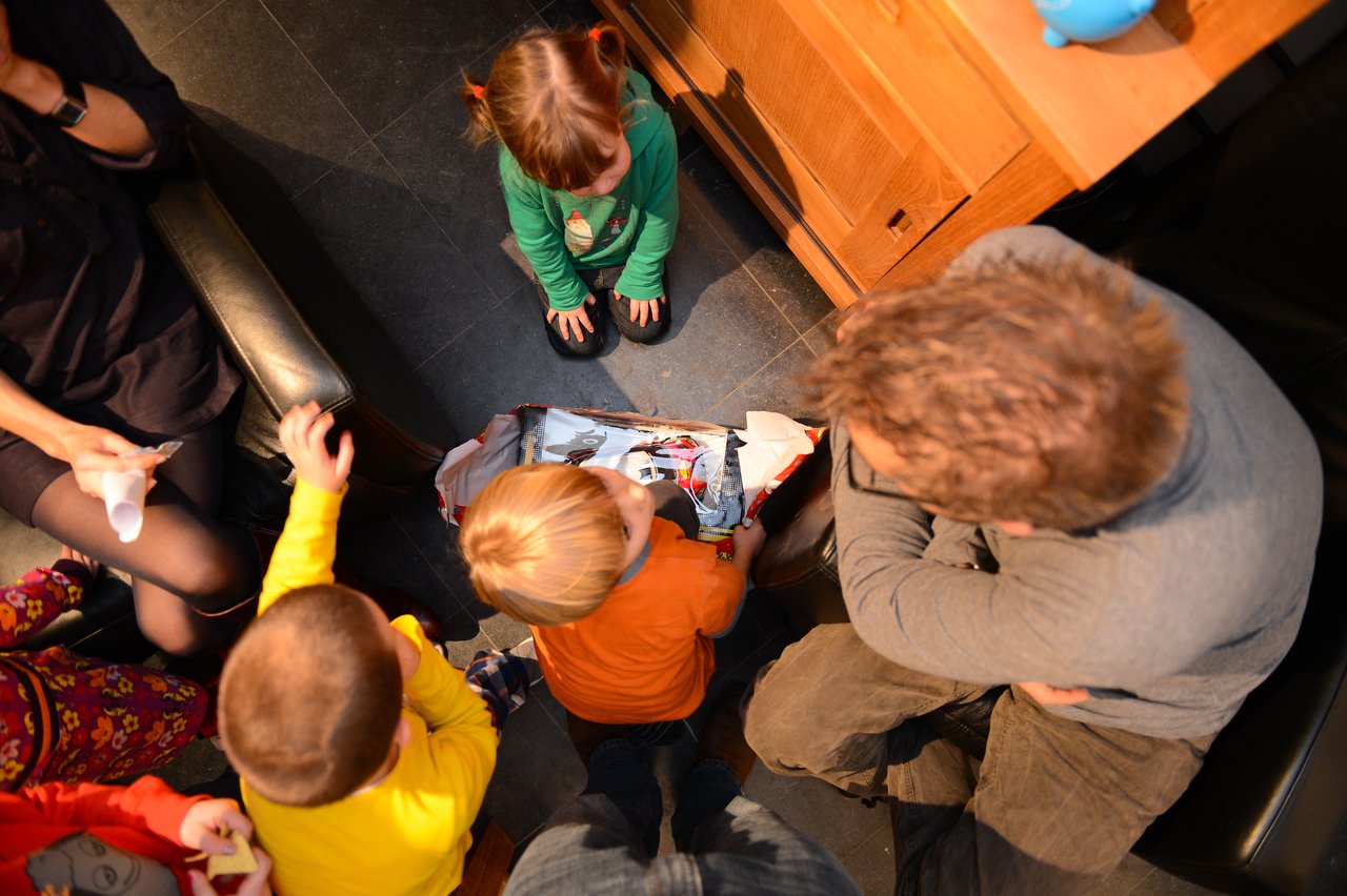 Children and an adult gather around an open gift bag, looking inside with curiosity at a party.