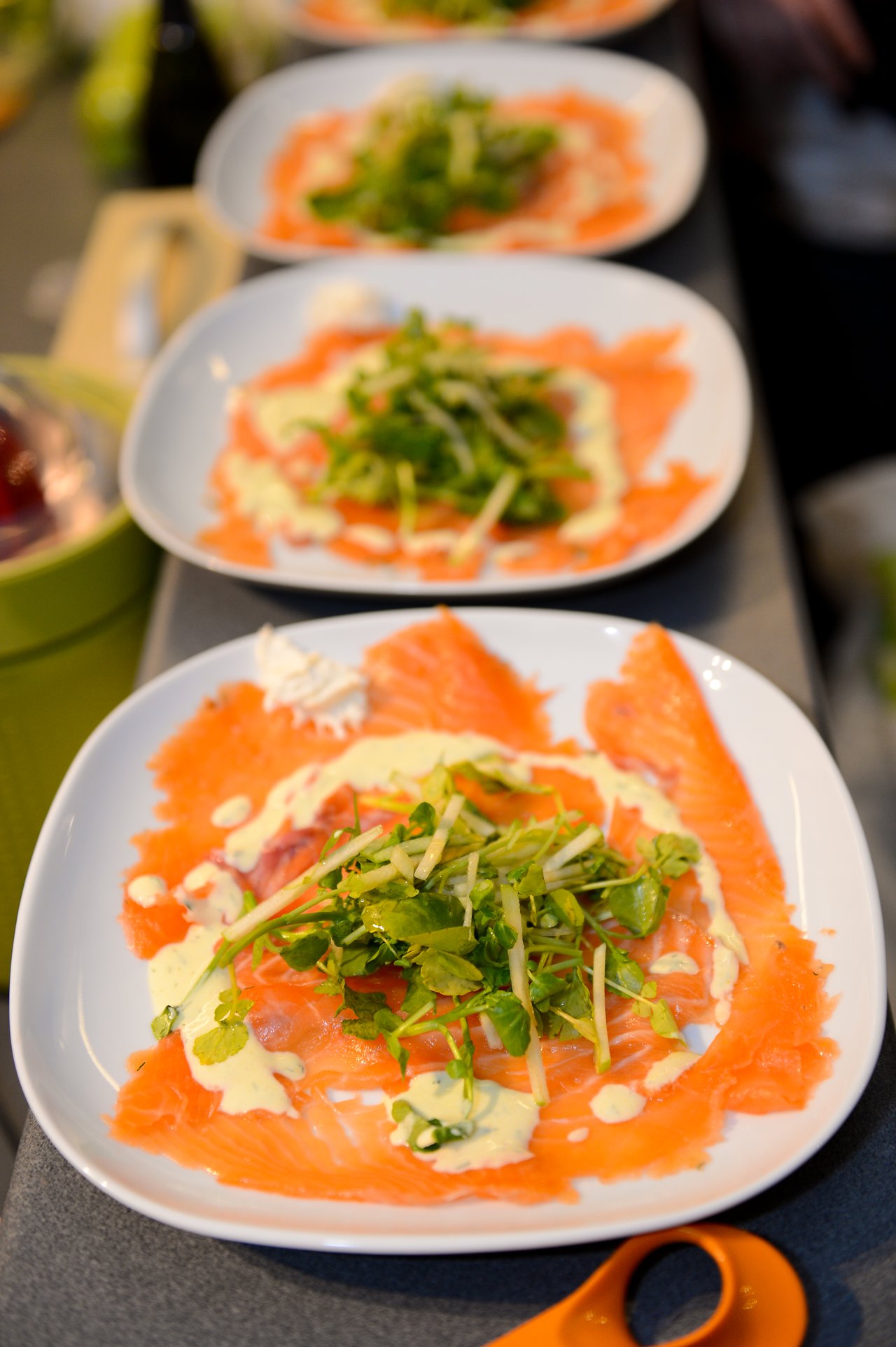 Plates of smoked salmon with greens and sauce are arranged on a table, ready to be served at a party.
