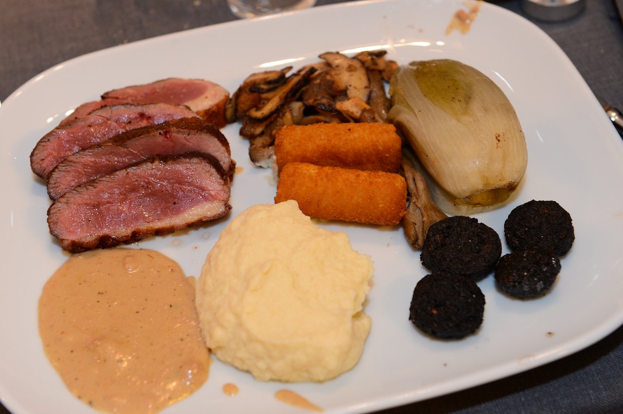 A plate with sliced meat, mashed potatoes, croquettes, mushrooms, black pudding, endive, and sauce at a New Year's Eve party.