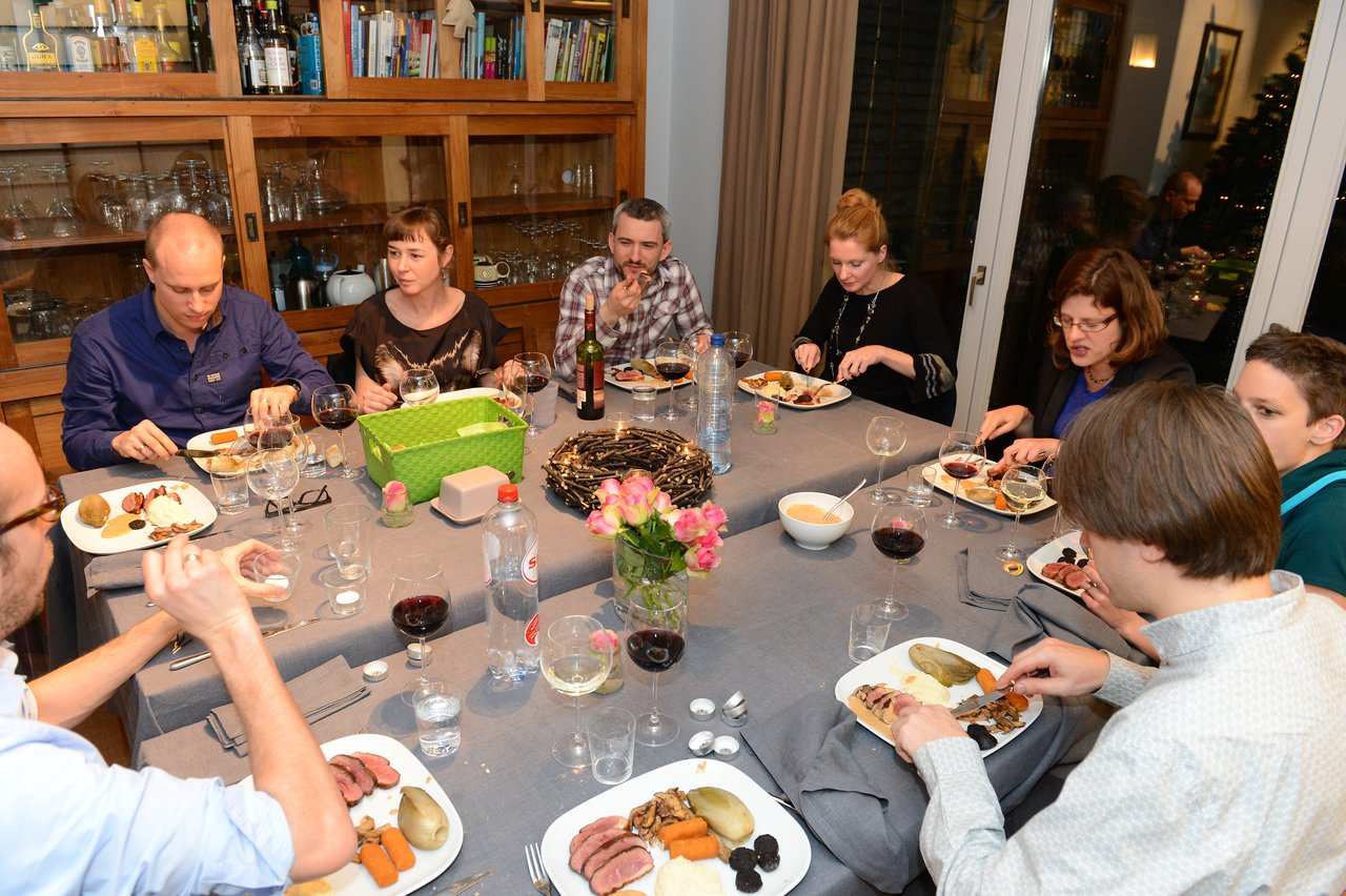 A group of people gathered around a table, eating dinner and drinking wine at a New Year's Eve party.