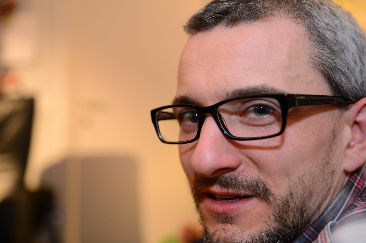 A man with glasses and a beard looks toward the camera at a New Year's Eve party.