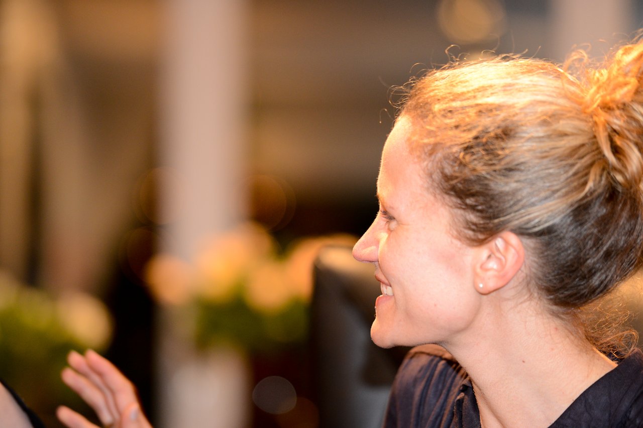 A woman with tied-back hair smiles and gestures while talking to someone at a New Year's Eve party.