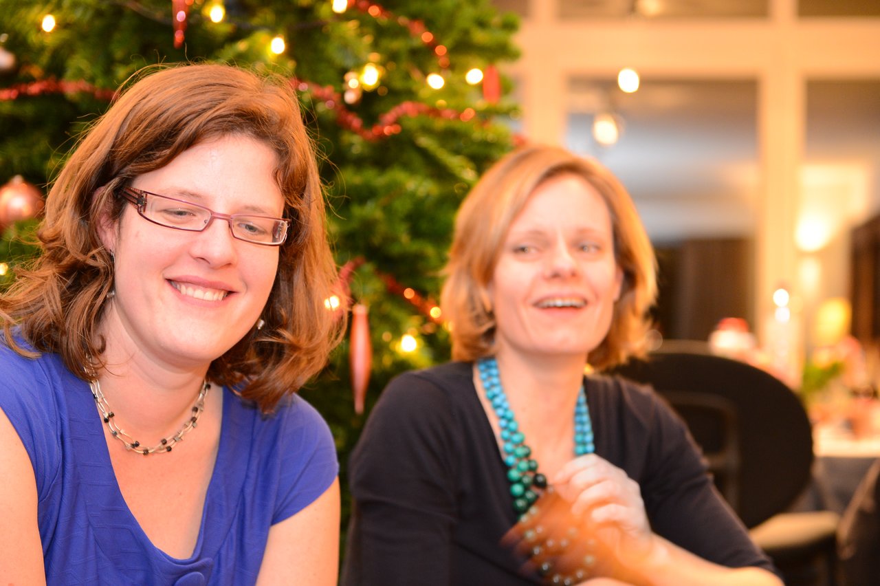 Two women smiling and enjoying a New Year's Eve party, with a decorated Christmas tree in the background.