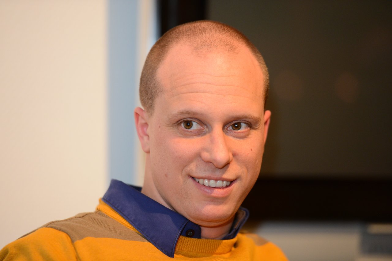 A man in a yellow sweater smiles at the camera during a New Year's Eve party.