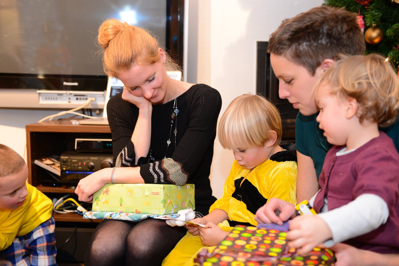 A young child in a yellow outfit reads a letter while surrounded by family members and presents.
