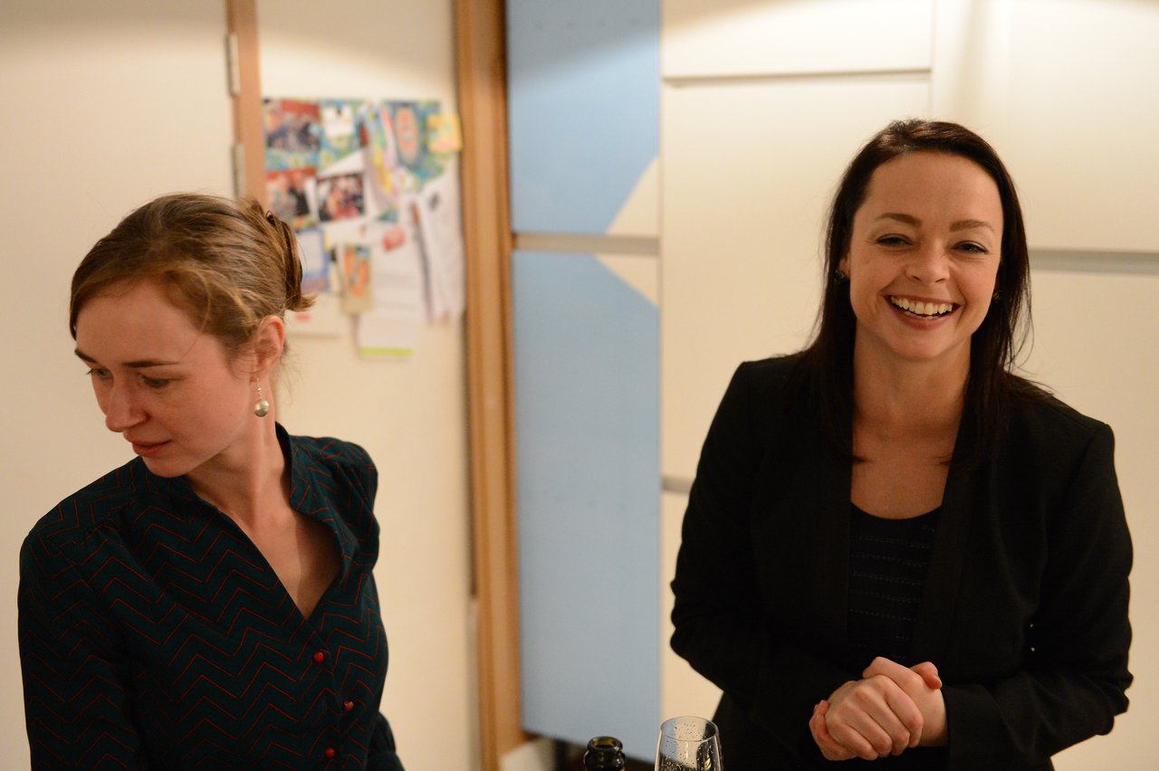 Two women at a New Year's Eve party, one smiling and the other looking away near a table with drinks.