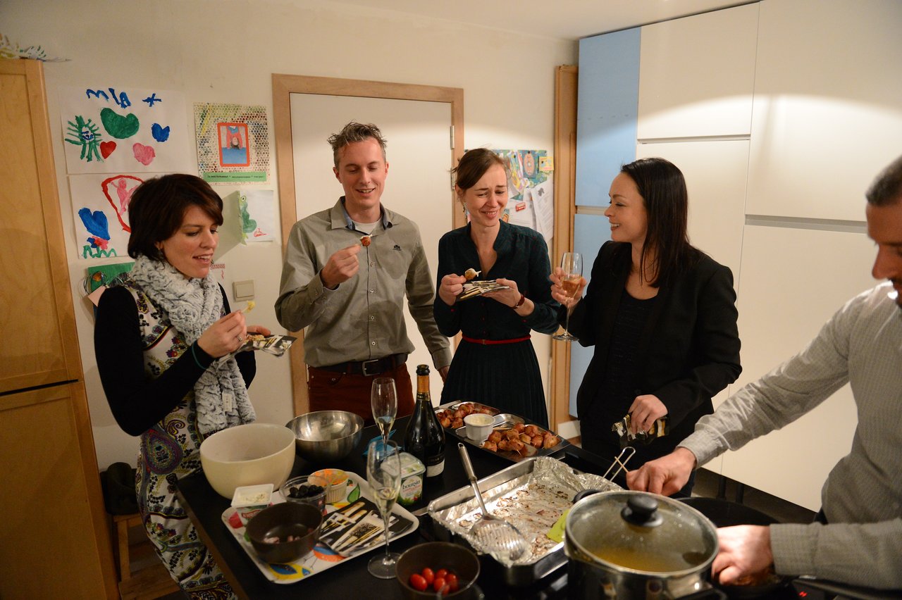 A group of people in a kitchen enjoying food and drinks at a New Year's Eve party.