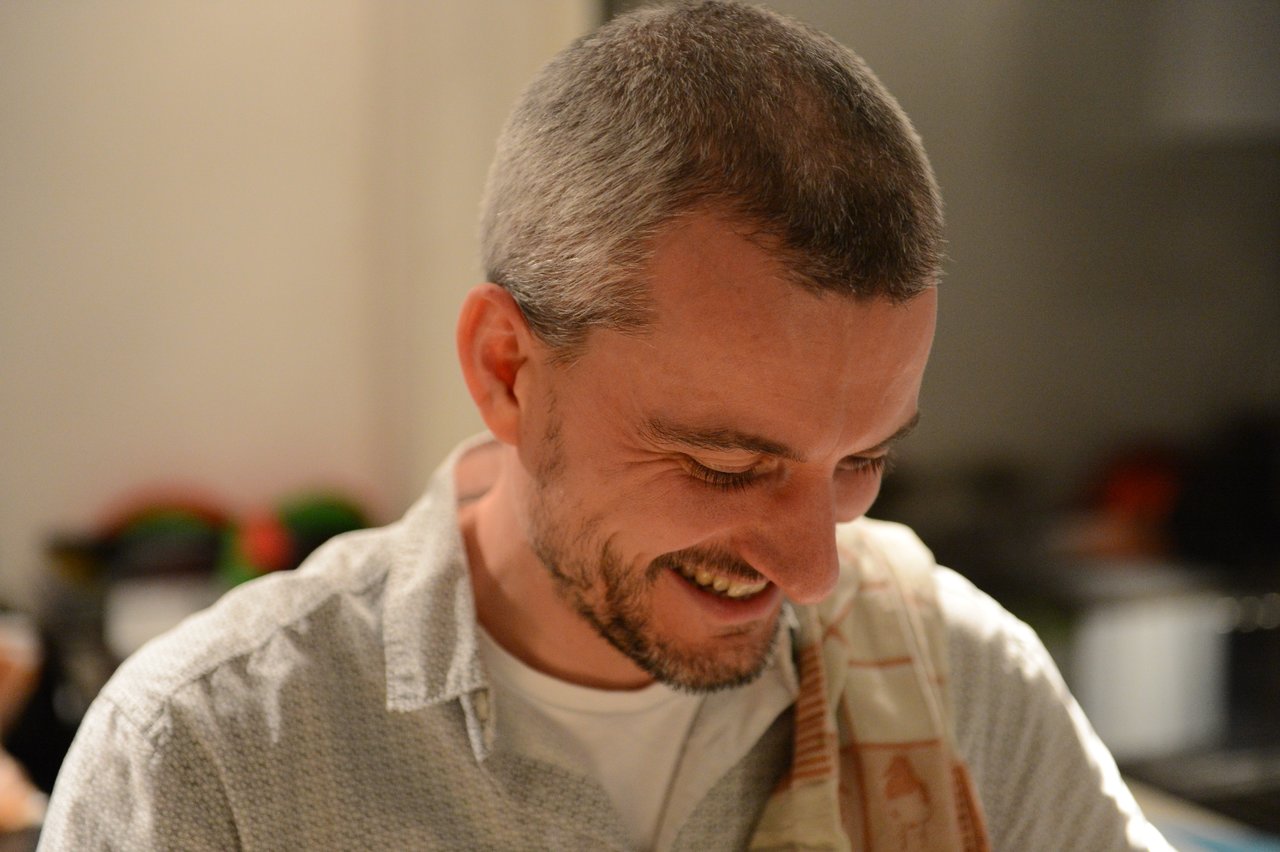 A man with short hair and a beard smiles while looking down at something during a party.