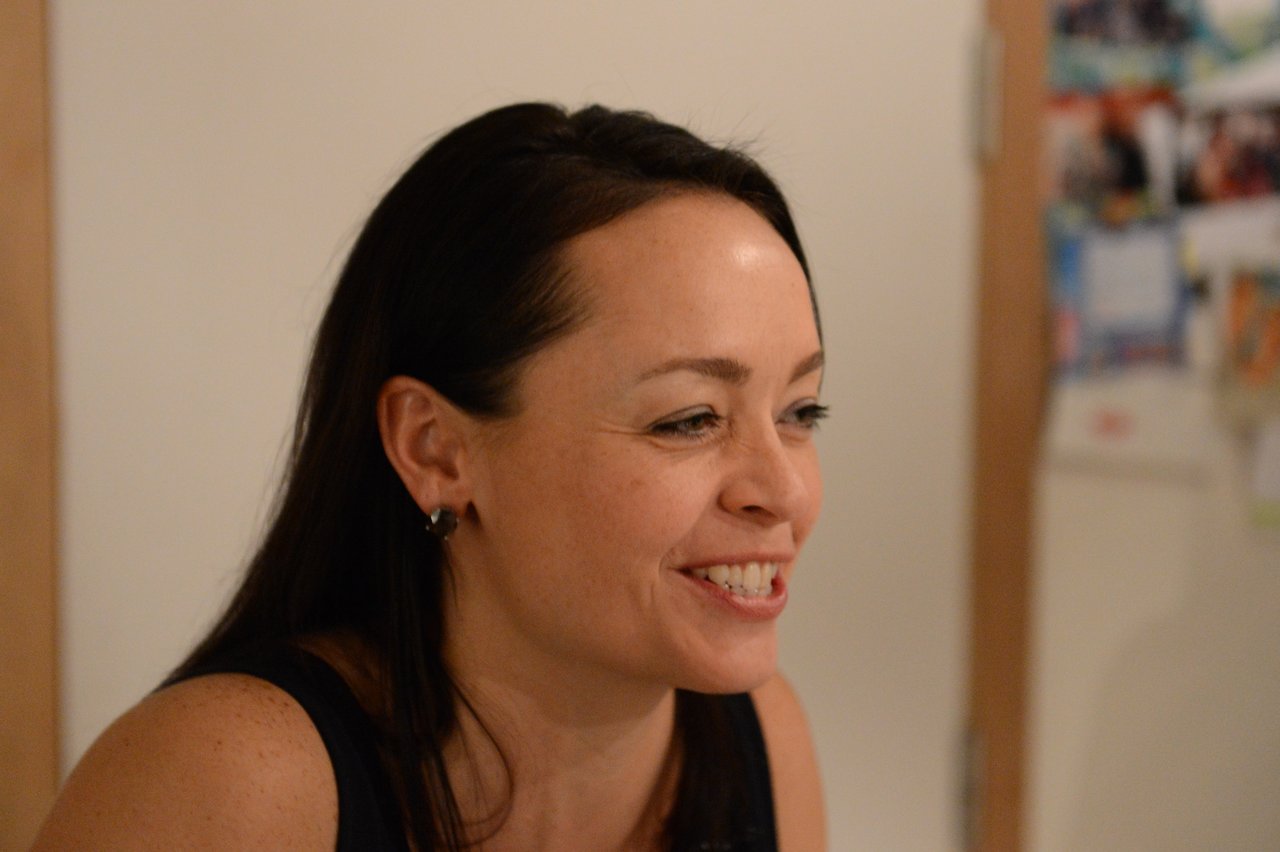 A woman with long dark hair smiles while talking at a New Year's Eve party.