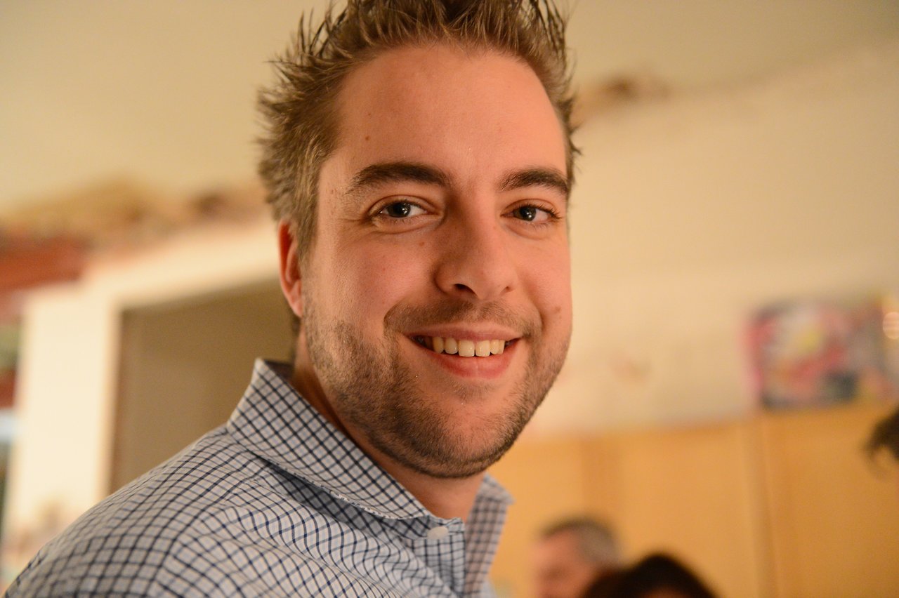 A man in a checkered shirt smiles at the camera during a New Year's Eve party.