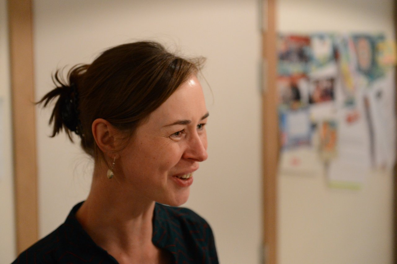 A woman with dark hair tied back smiles while talking at an indoor New Year's Eve party.