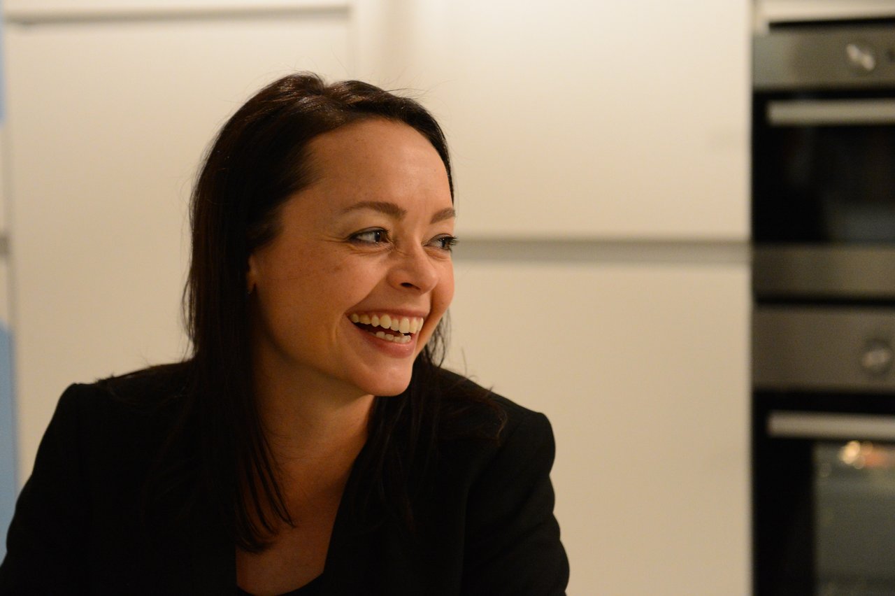 A woman in a black outfit smiles and laughs at a New Year's Eve party.