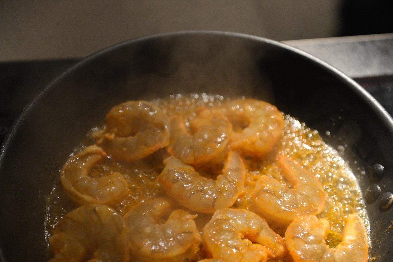 Shrimp cooking in a hot pan with bubbling oil, releasing steam.