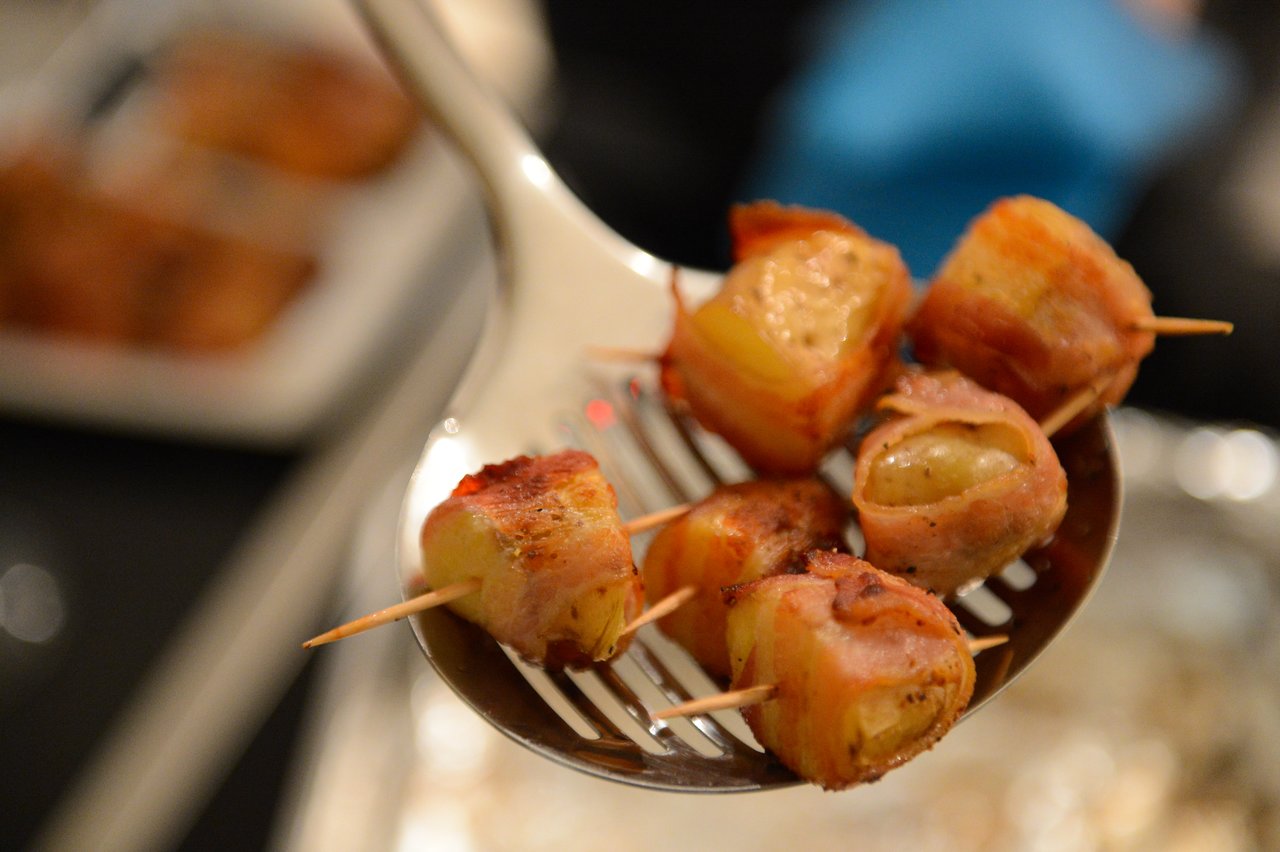 A slotted spoon holds bacon-wrapped appetizers with toothpicks, freshly cooked and ready to be served at a party.