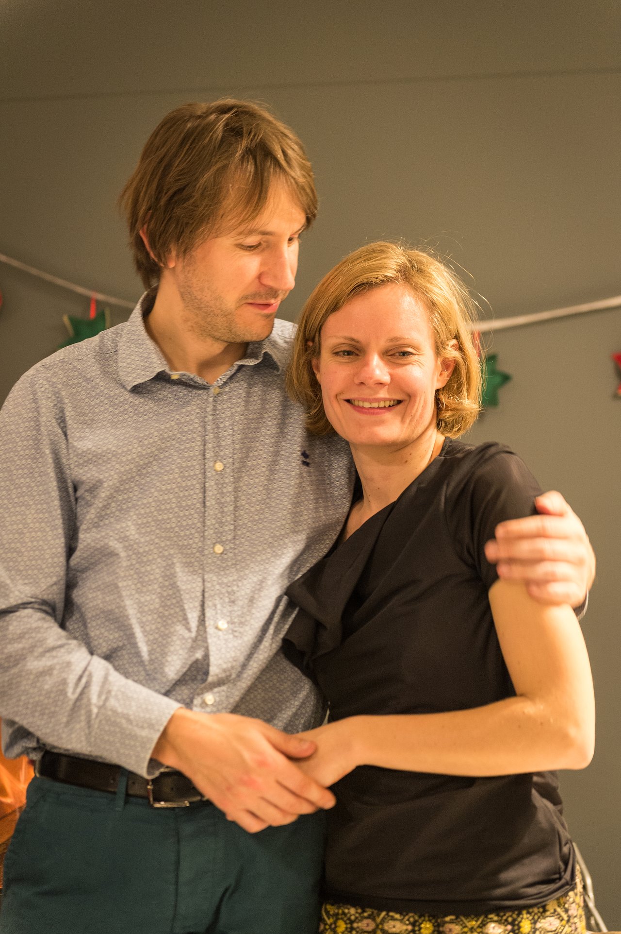 A man and woman stand close together, smiling and embracing at a New Year's Eve party.
