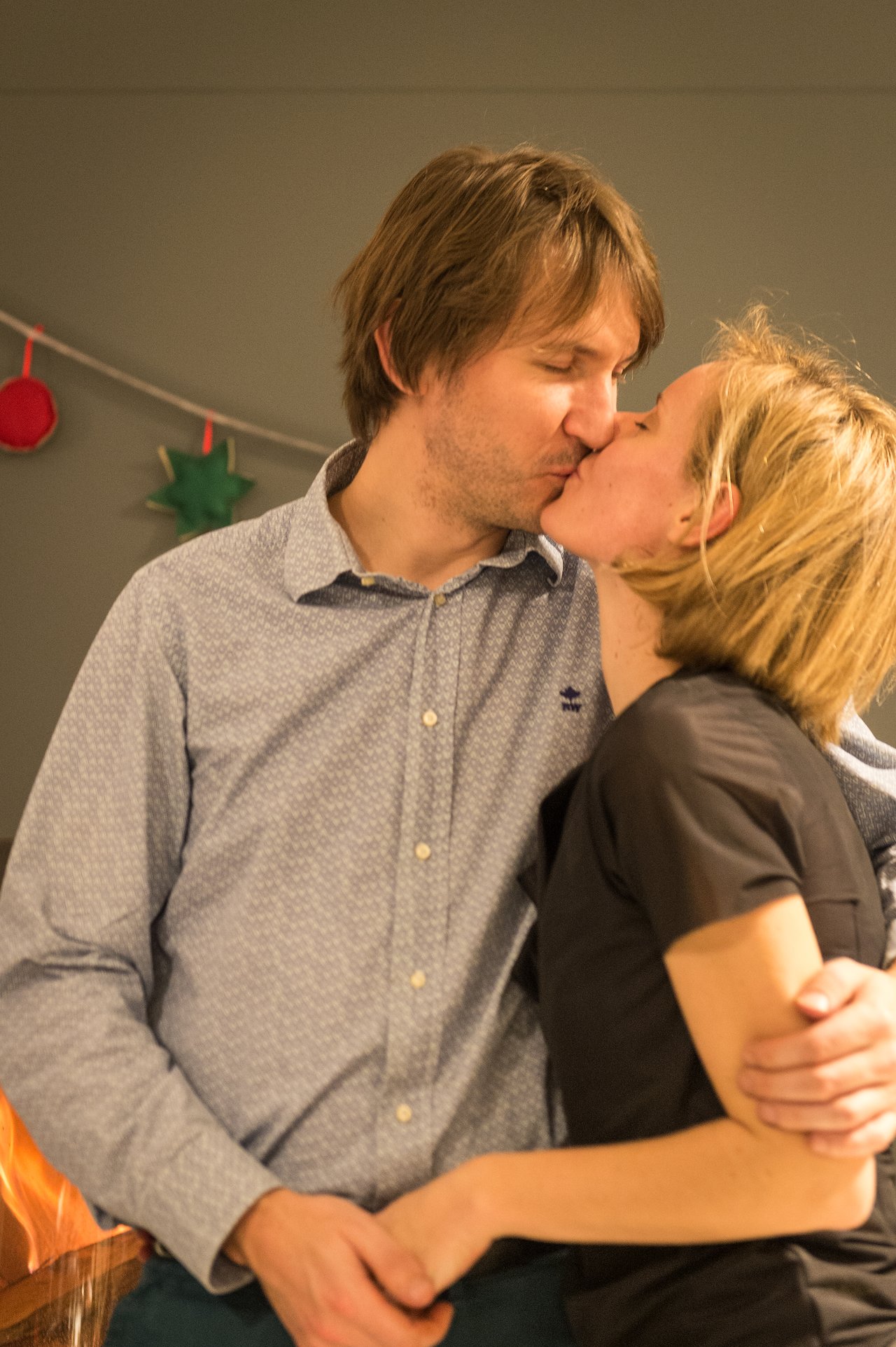 A couple shares a kiss at a New Year's Eve party, embracing each other closely.