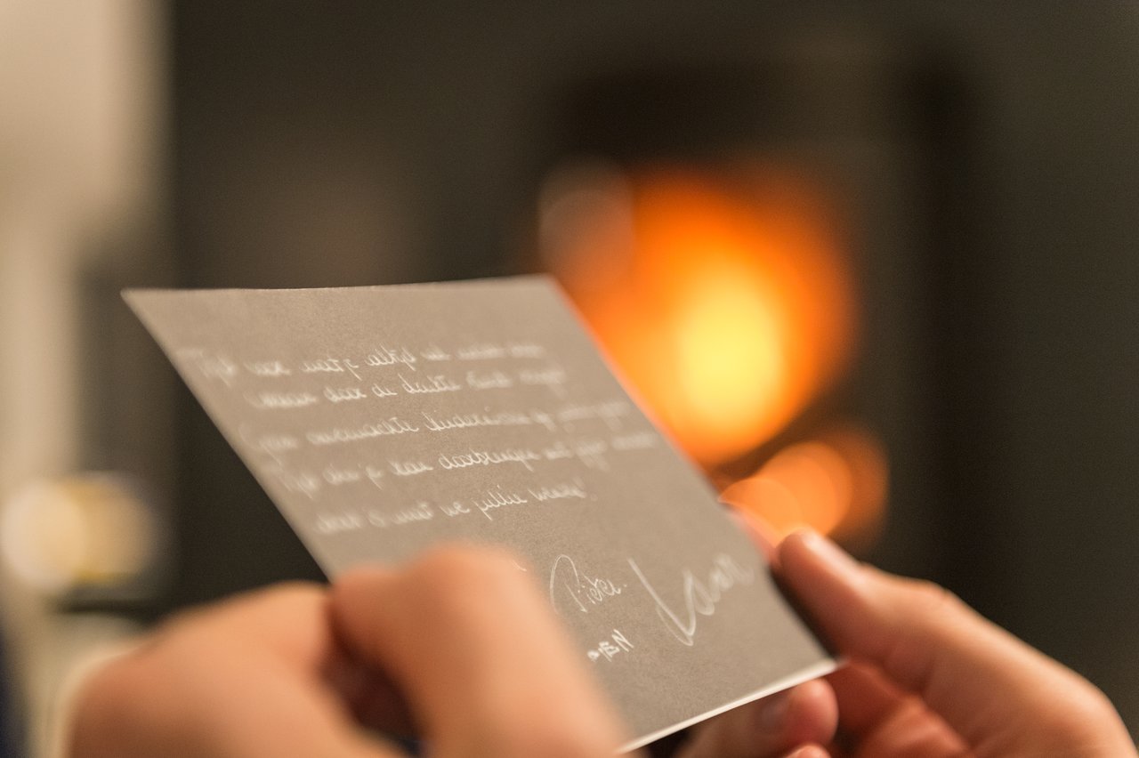 A person holds and reads a handwritten card near a warm, glowing fireplace.