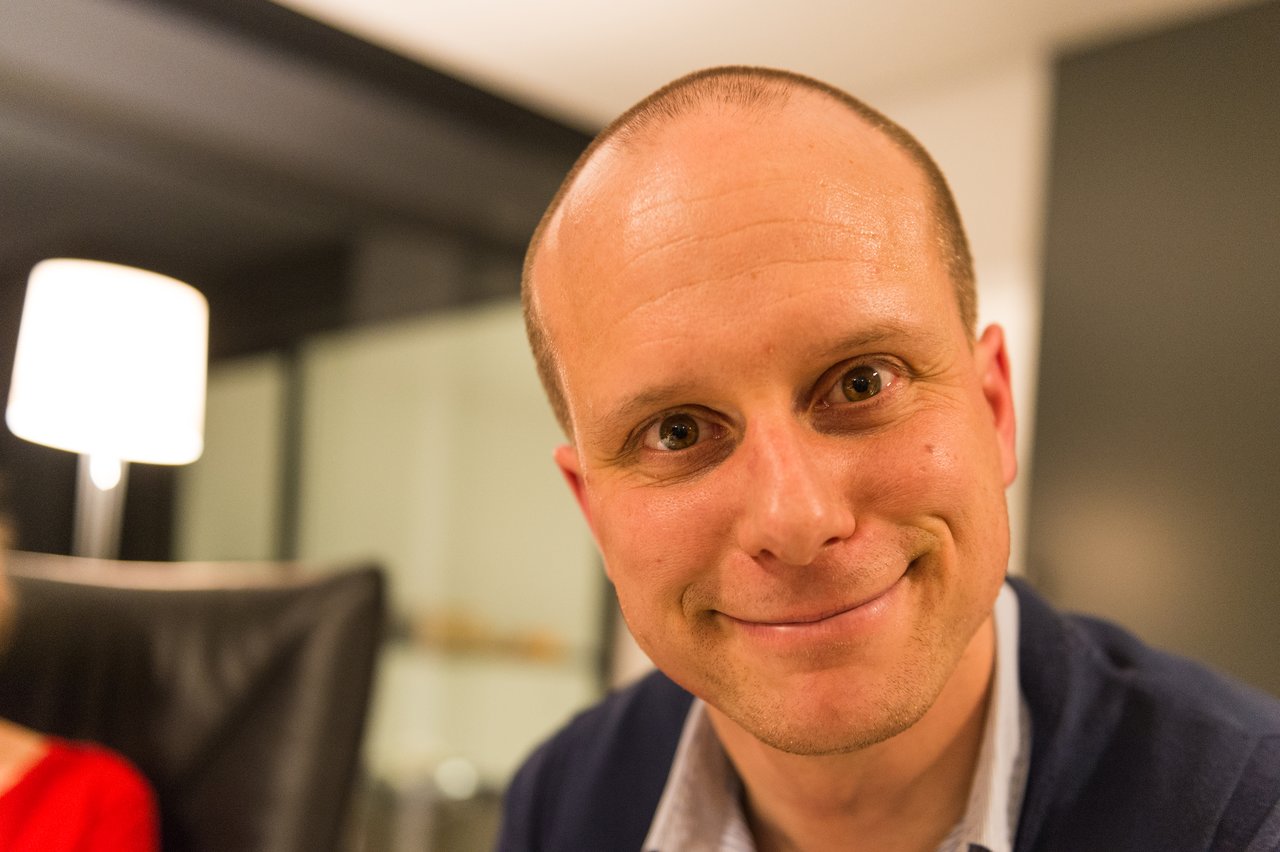 A man in a dark sweater smiles closely at the camera during a New Year's Eve party.