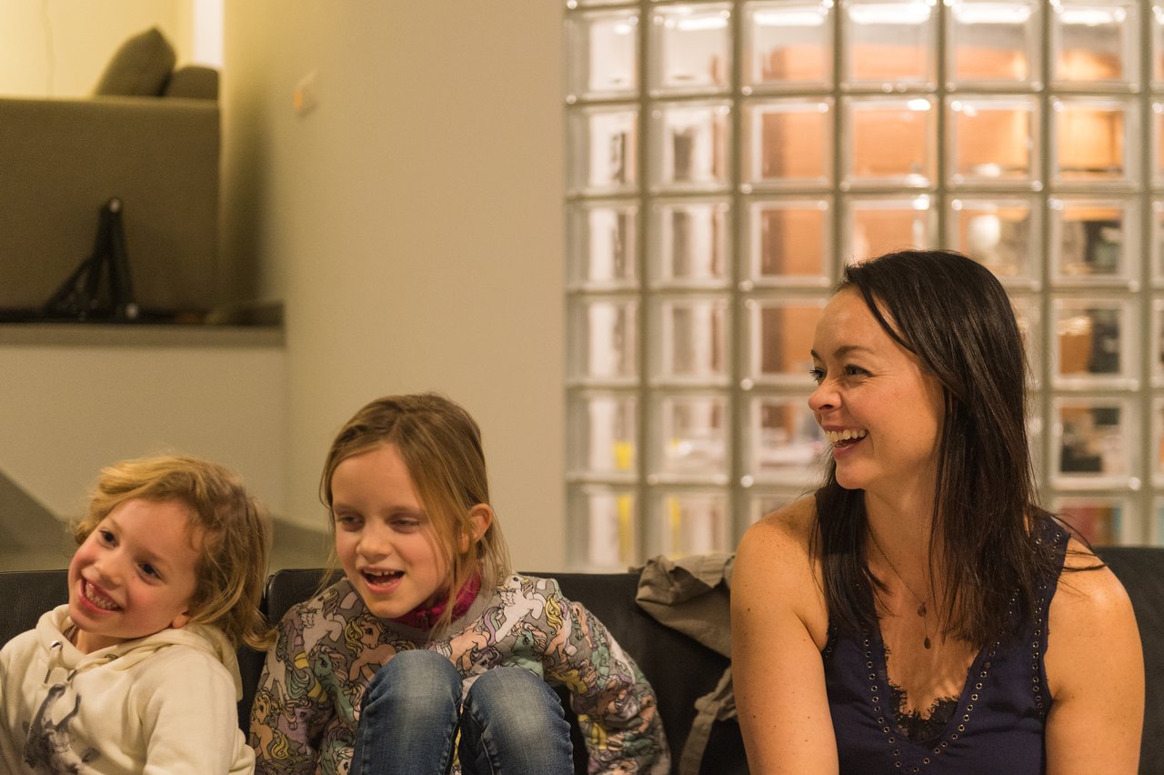 A woman and two children sit on a couch, smiling and laughing together at a New Year's Eve party.