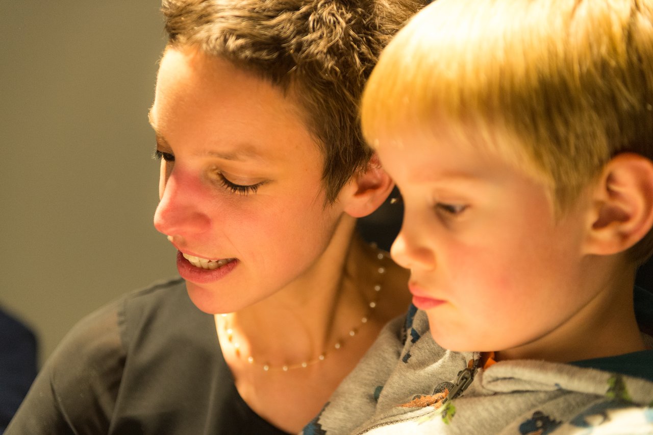 A woman and a young child sit closely together, both focused on something in front of them.