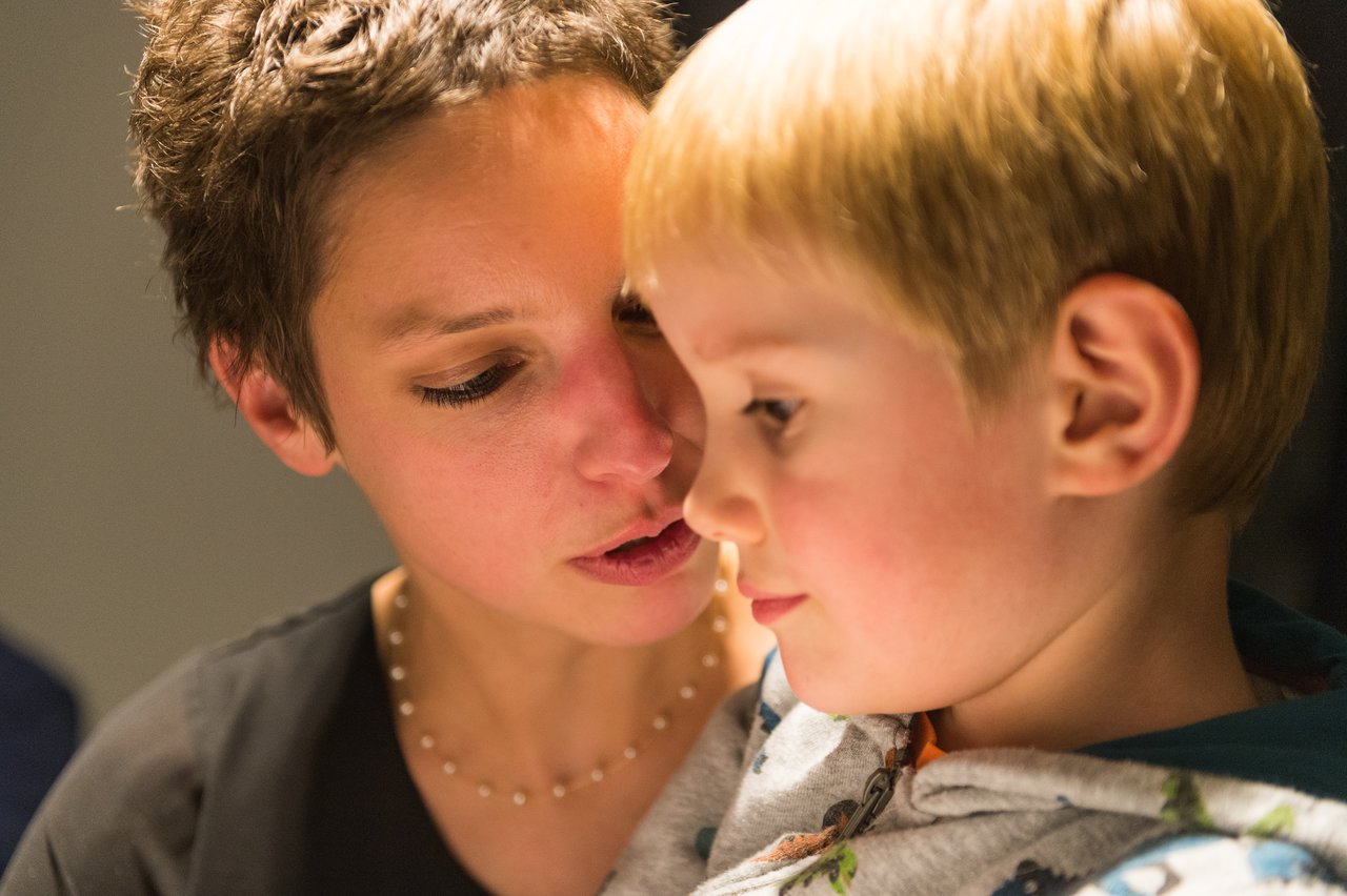 A woman leans in close to a young child, speaking softly while the child listens attentively.