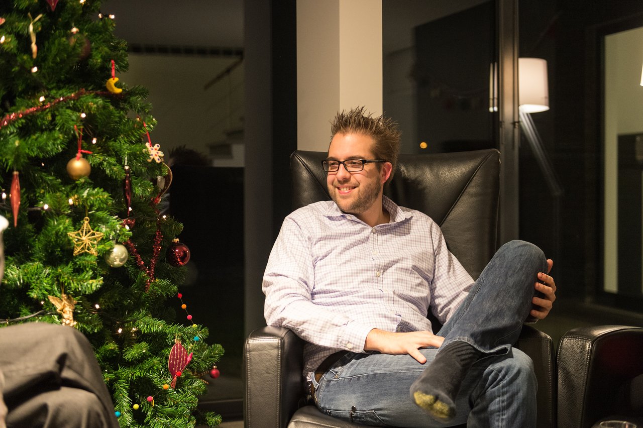 A man wearing glasses sits in a chair, smiling and talking.