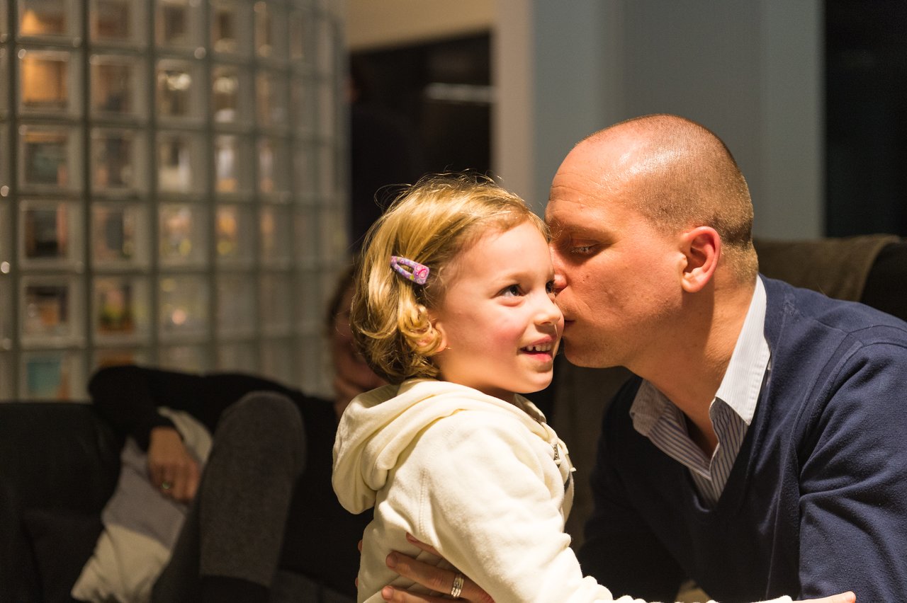 A man in a blue sweater kisses a smiling young girl on the cheek at a party.