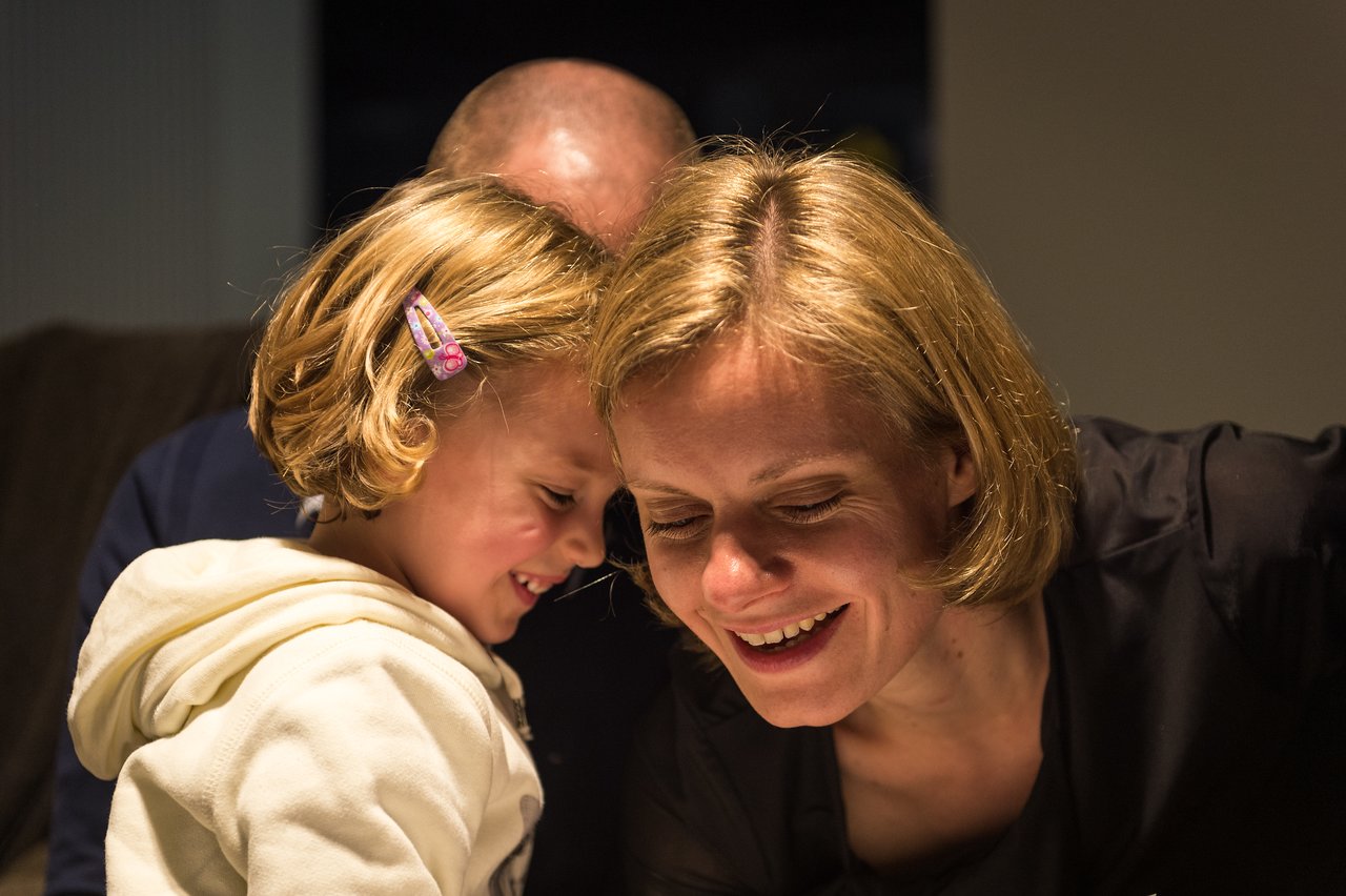 A young girl and a woman smile as they lean in close, sharing a happy moment at a party.