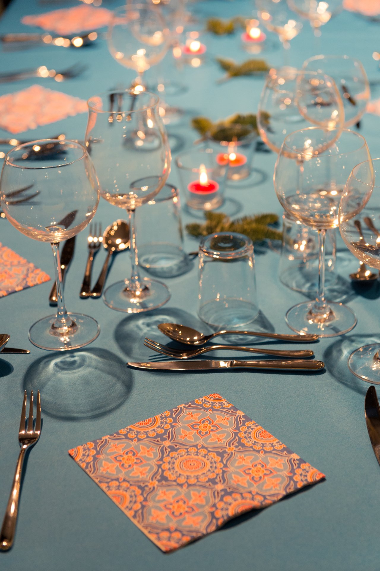 A festive dinner table set with wine glasses, silverware, patterned napkins, and candles for a New Year's Eve party.
