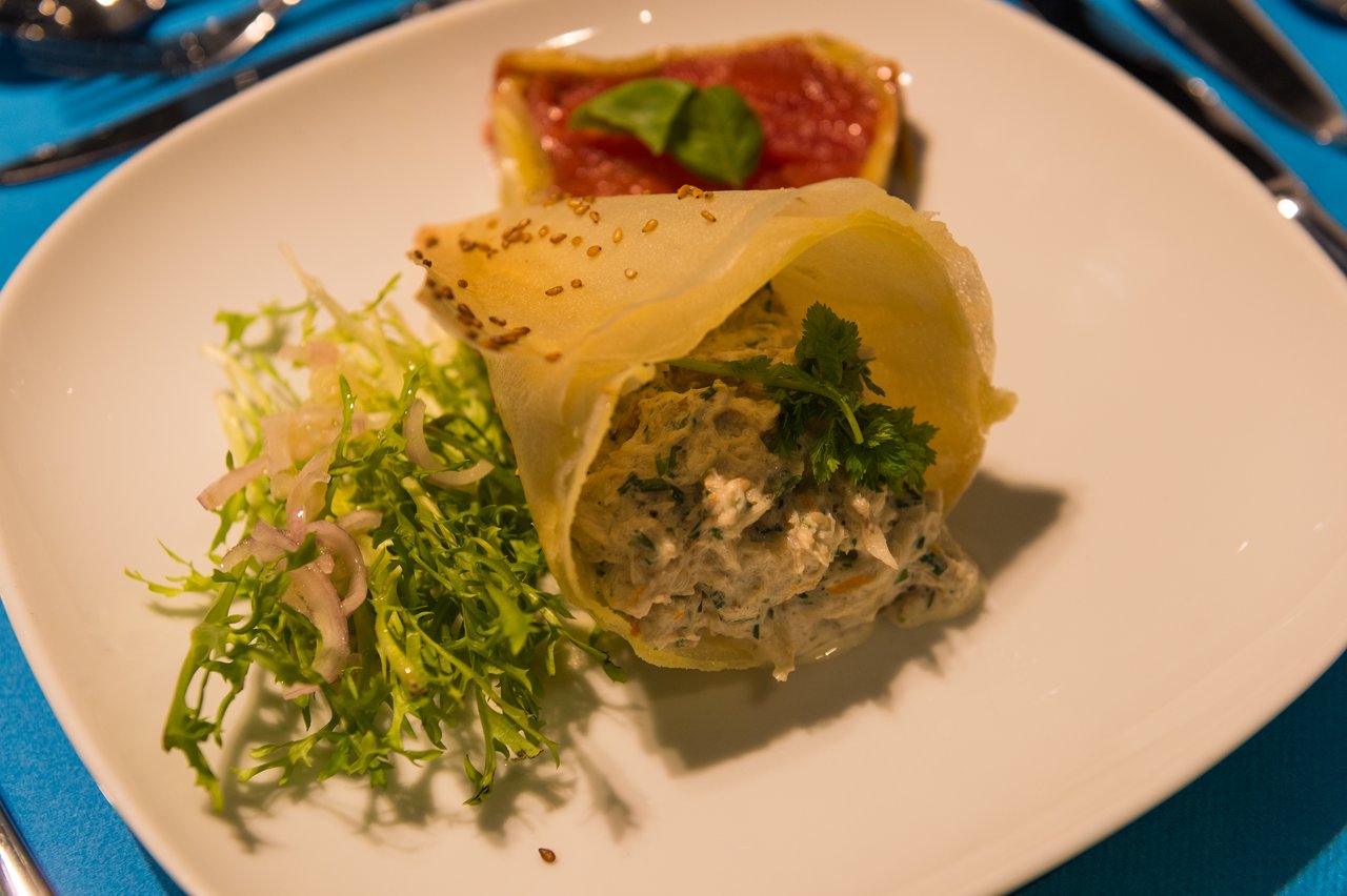 A plated dish with a crispy shell filled with creamy filling, garnished with herbs, served with salad and grapefruit.