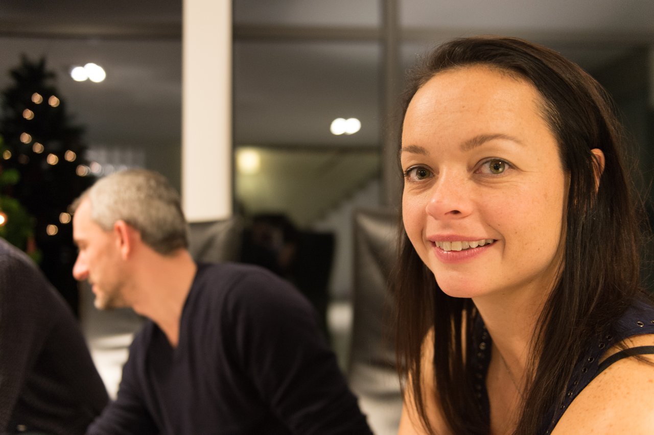 A woman smiles at the camera while a man in the background talks to someone at a New Year's Eve party.