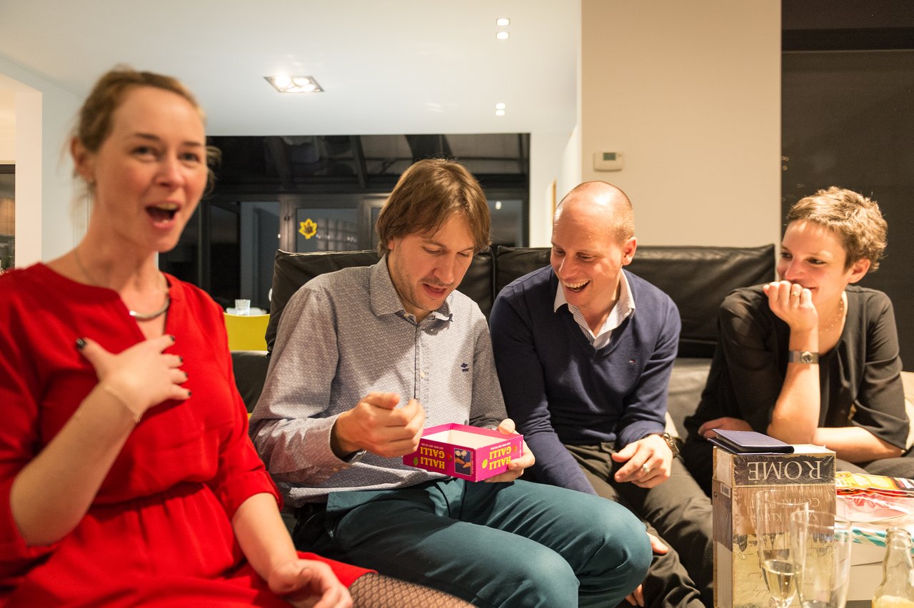 A group of four people sitting together, laughing and reacting as one person opens a party game box.