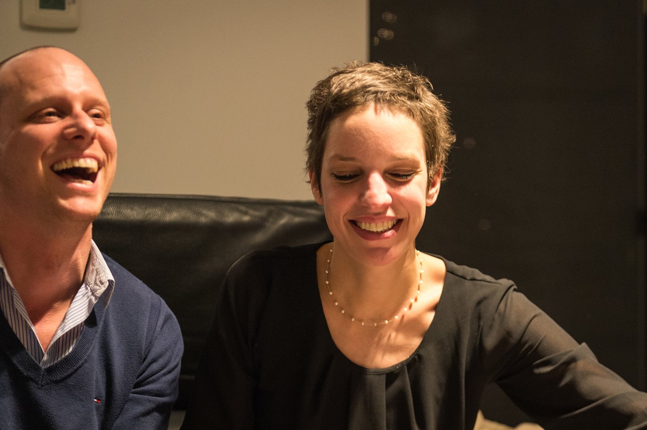 Two people smiling and laughing at a New Year's Eve party, sitting close together in a relaxed setting.